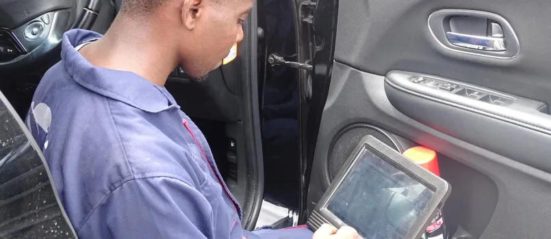 A mechanic at DOHC Auto in Nairobi uses a tablet to diagnose a Honda engine issue, with an ABCDEF guide on the screen