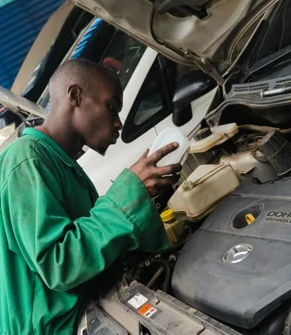 Mechanic in Nairobi inspecting fluid levels under the hood of a Mazda vehicle