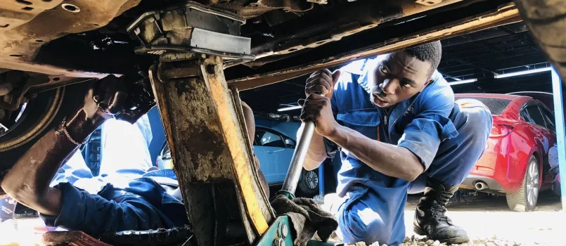 Mechanic in Nairobi working under a vehicle with a jack and tools during a maintenance check